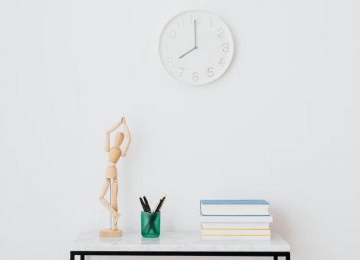 A minimalist workspace setup featuring books, a clock, and decorative elements on a white wall.
