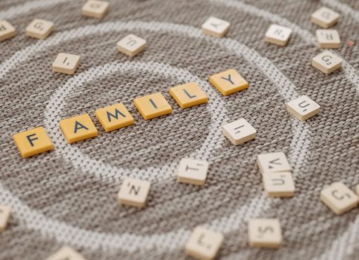 An artistic display of Scrabble tiles spelling 'FAMILY' on a textured carpet surface.